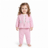 A toddler girl with curly light brown hair stands barefoot against a plain white background, wearing a pink two-piece outfit consisting of a long-sleeve button-front cardigan with white bow details and matching pink pants.