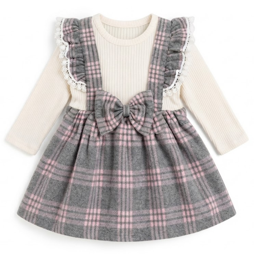 A toddler girl's long-sleeve dress featuring a cream ribbed knit top and a gray plaid pinafore-style skirt with ruffled shoulder straps and a large bow at the waist.