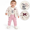 A baby wearing a cream floral cardigan with a panda print, pink pants, and white shoes, standing against a white background. Two circular detail insets on the right show close-ups of the cardigan's floral pattern and the dark burgundy bow accent.