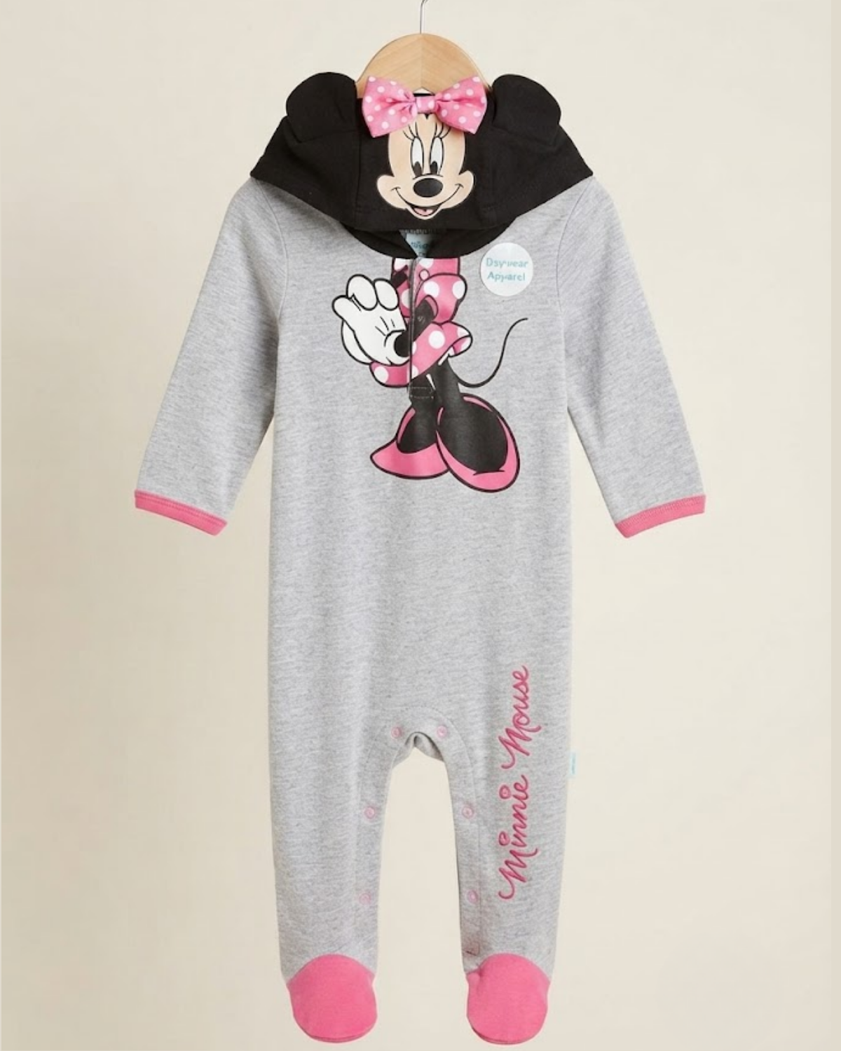 A baby footed one-piece sleeper in heather gray, featuring a large Minnie Mouse graphic on the chest, a black hood with Minnie Mouse's face and a pink bow, pink cuffs, and pink toe caps. The word 'Minnie Mouse' is printed vertically on the leg.