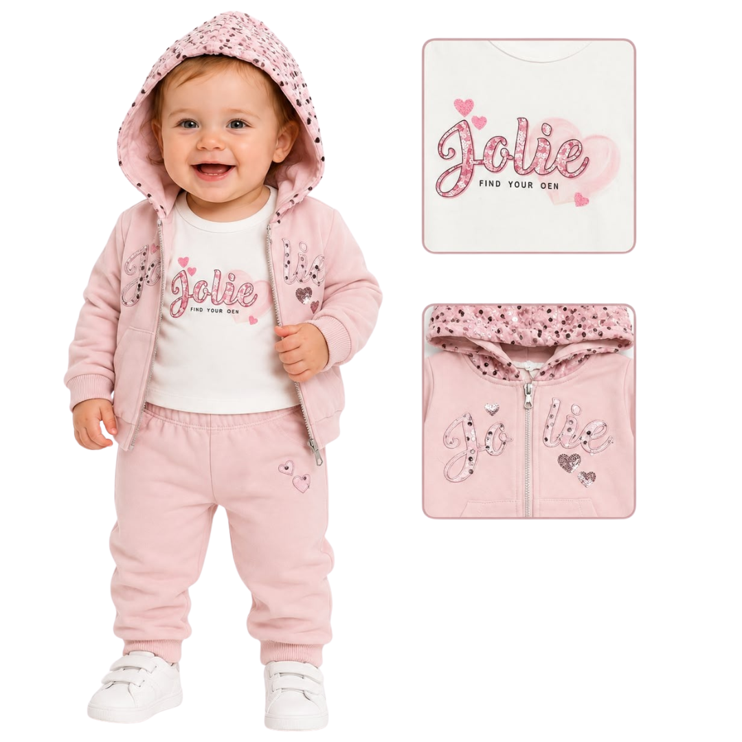 A baby girl wearing a pink two-piece tracksuit with a white t-shirt underneath. The set includes a zip-up hoodie with a hood, matching jogger pants, and a matching square washcloth.
