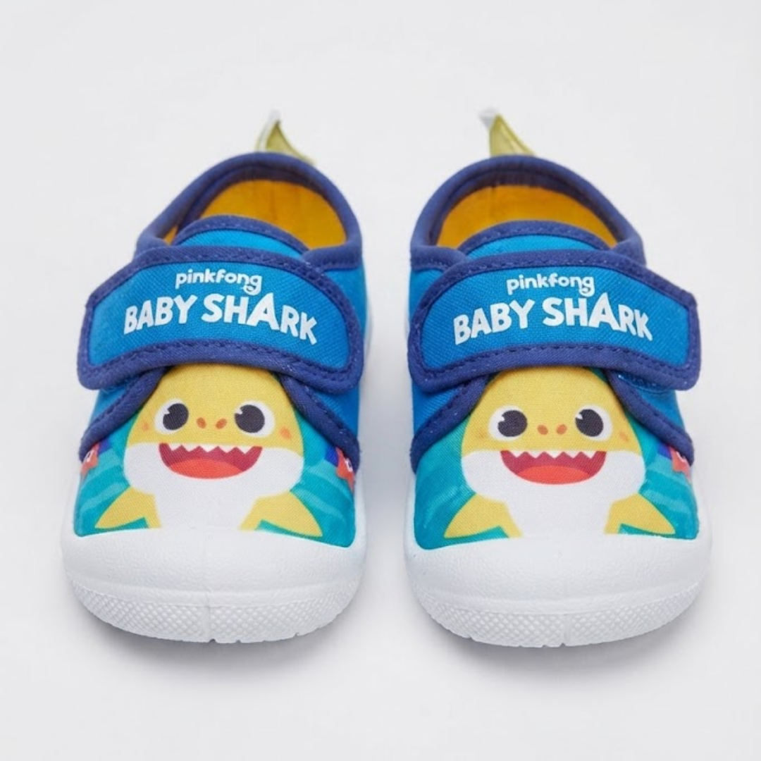 A pair of Pinkfong Baby Shark toddler slip-on shoes with blue straps, yellow and white shark graphics, and white soles, shown against a plain white background.