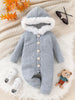 Gray quilted baby romper with white fur trim on a textured surface with shoes and a teddy bear.