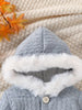 Gray hooded coat with white fur trim on a textured beige surface with autumn leaves.