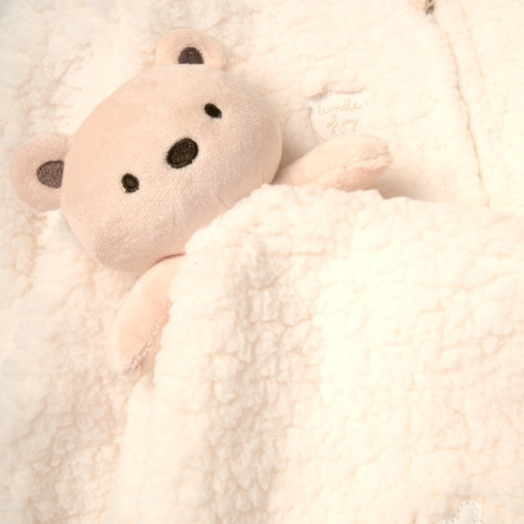 

Close-up detail of a soft cream plush teddy bear toy resting against cozy fleece fabric with a 