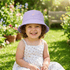 Child wearing a purple bucket hat and white dress sitting in a garden.