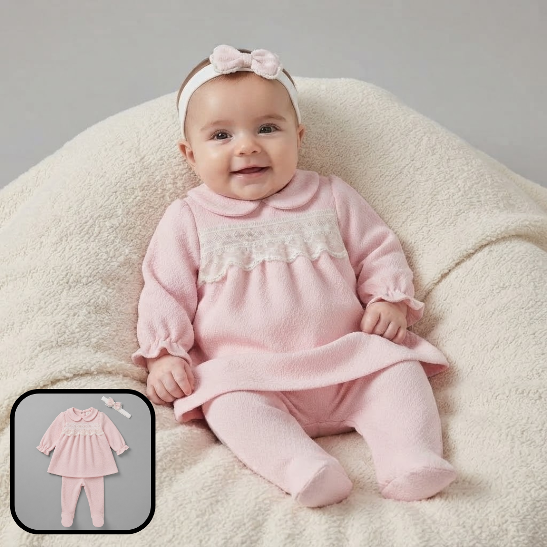 A baby wearing a pink footed romper with a lace chest detail, matching pink leggings, and a pink bow headband, sitting on a cream-colored textured cushion. A small inset in the bottom-left corner shows the romper laid flat.