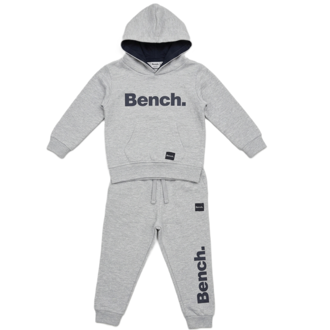 A two-piece kids' tracksuit from the brand Bench, featuring a light gray heathered hoodie with a dark navy hood lining and 'Bench.' printed across the chest, paired with matching jogger pants that have a vertical 'Bench.