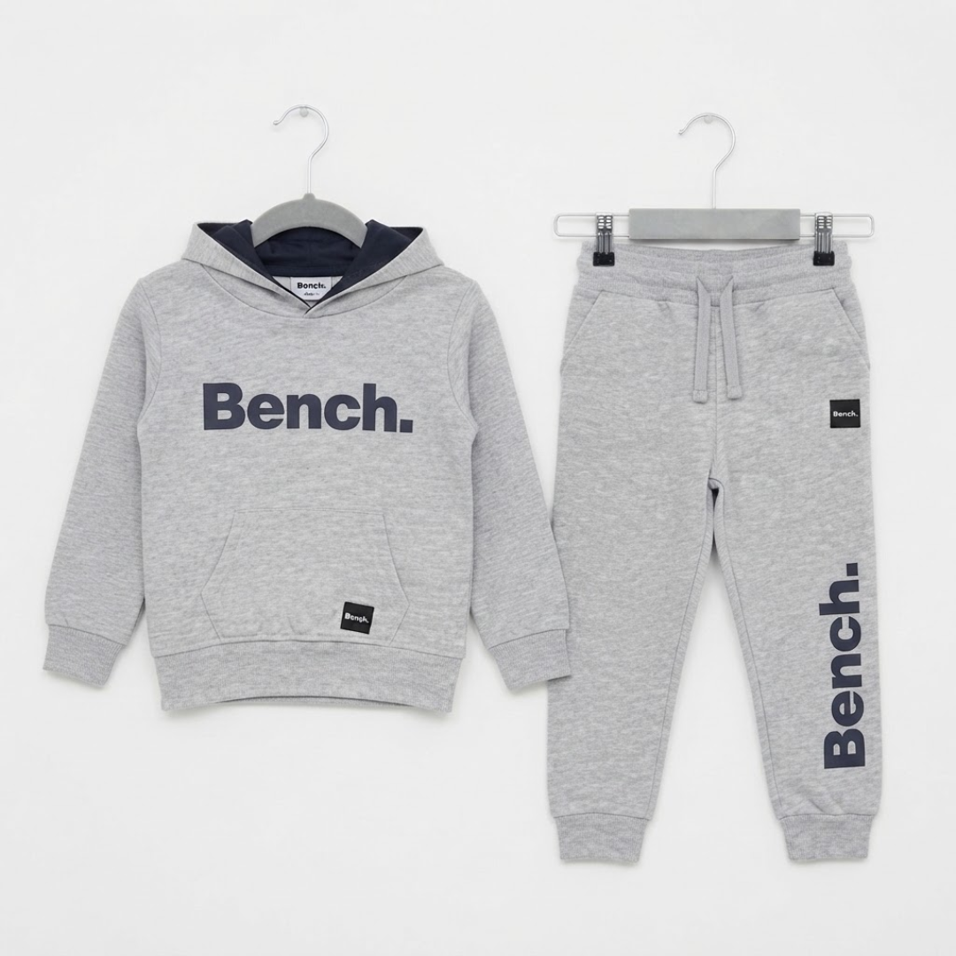 A children's two-piece lounge set from Bench, featuring a heather gray hoodie with a navy blue hood lining and 'Bench.' logo on the chest, paired with matching heather gray joggers with a drawstring waist, 'Bench.