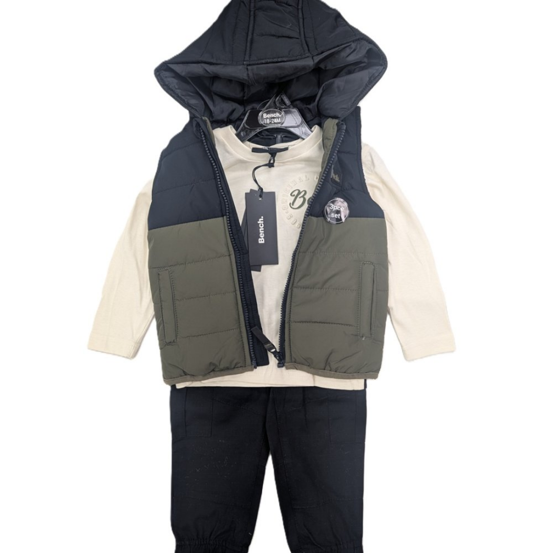 A children's hooded puffer vest layered over a cream long-sleeve shirt and black pants, shown on a hanger against a plain white background. The vest has a dark navy upper section and hood, an olive green lower section, and a black zipper.