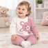 A baby girl wearing cream and pink waffle outfit set for babies aged 9 to 24 months, with bear appliqué and matching trousers sitting on the floor