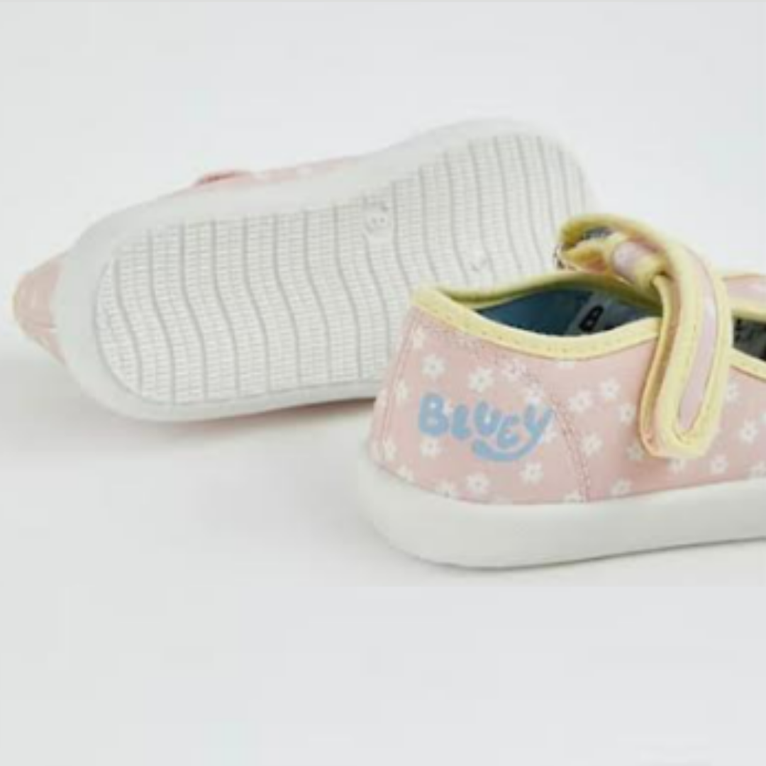 A pair of children's low-top canvas sneakers in light pink with a white floral pattern, featuring a yellow elastic strap closure and the brand name 'Bluey' printed in blue on the side, shown against a plain white background.