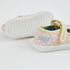 A pair of children's low-top canvas sneakers in light pink with a white floral pattern, featuring a yellow elastic strap closure and the brand name 'Bluey' printed in blue on the side, shown against a plain white background.
