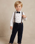 Young boy in formal attire with suspenders and a bow tie on a beige background