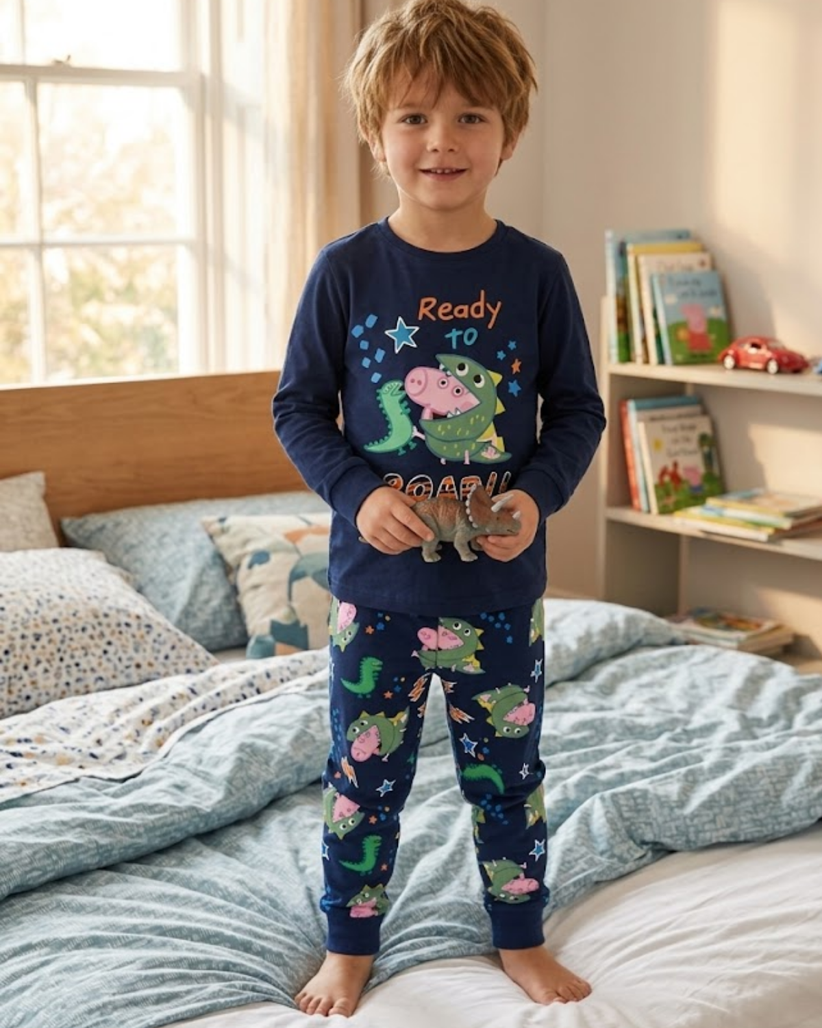 A boy wearing the Peppa Pig themed pyjama standing on the bed holding a toy.