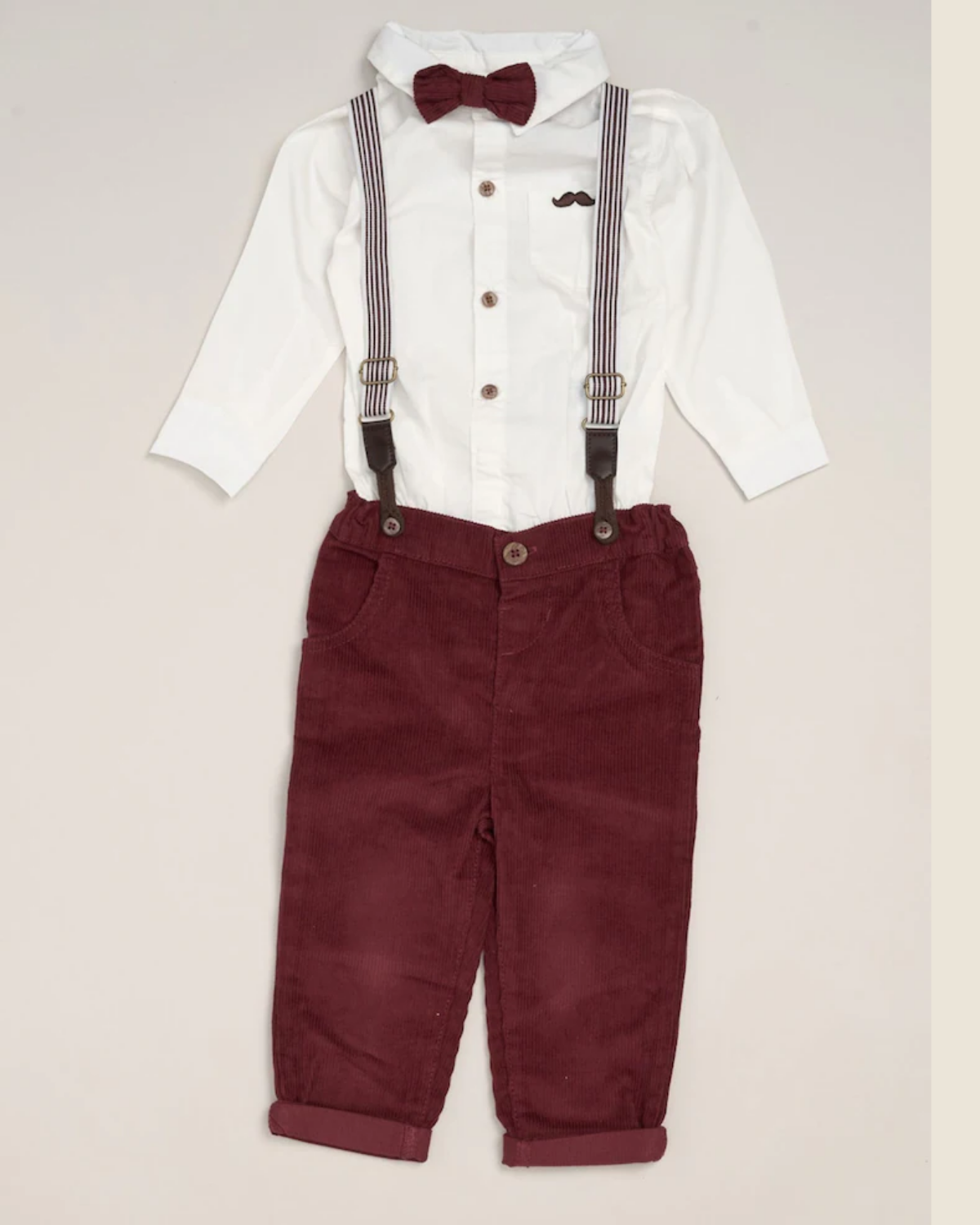 Children's outfit with white shirt, suspenders, maroon bow tie, and pants on a beige background