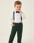 Child wearing a white shirt, green pants, suspenders, and a bow tie on a plain background