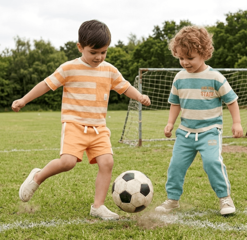 Two children playing soccer on a grass field with a goalpost in the background.