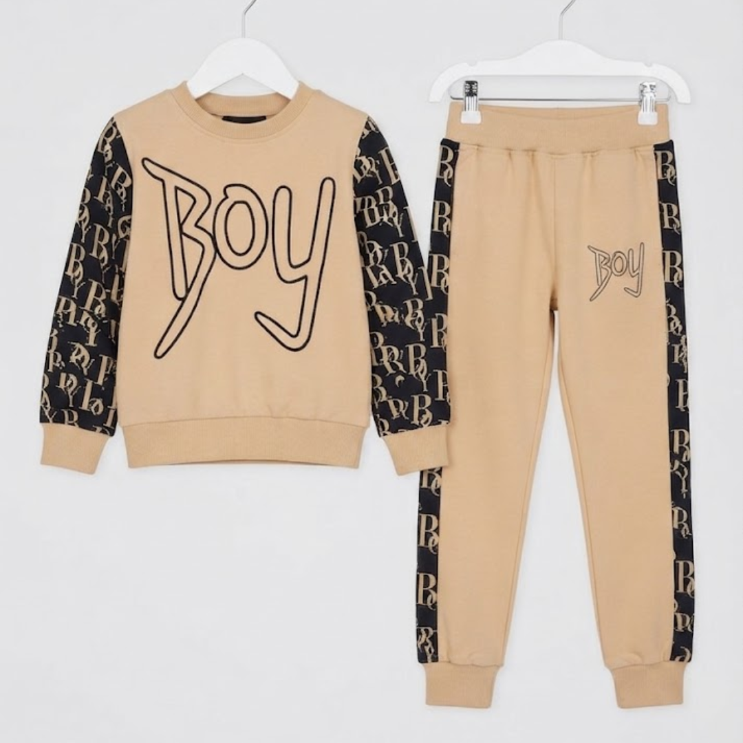 A two-piece kids' sweatshirt and jogger set in beige and black, hanging on white hangers against a white background. The sweatshirt features a beige body with black patterned sleeves and a large 'Boy' graphic on the chest.