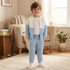 A young boy stands in a cozy living room wearing a light blue and white color-blocked zip-up jacket and matching sweatpants.