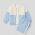 A children's two-piece tracksuit set featuring a color-blocked zip-up jacket and matching sweatpants. The jacket has a cream upper section, light blue lower sleeves and hem, and a white inner layer.