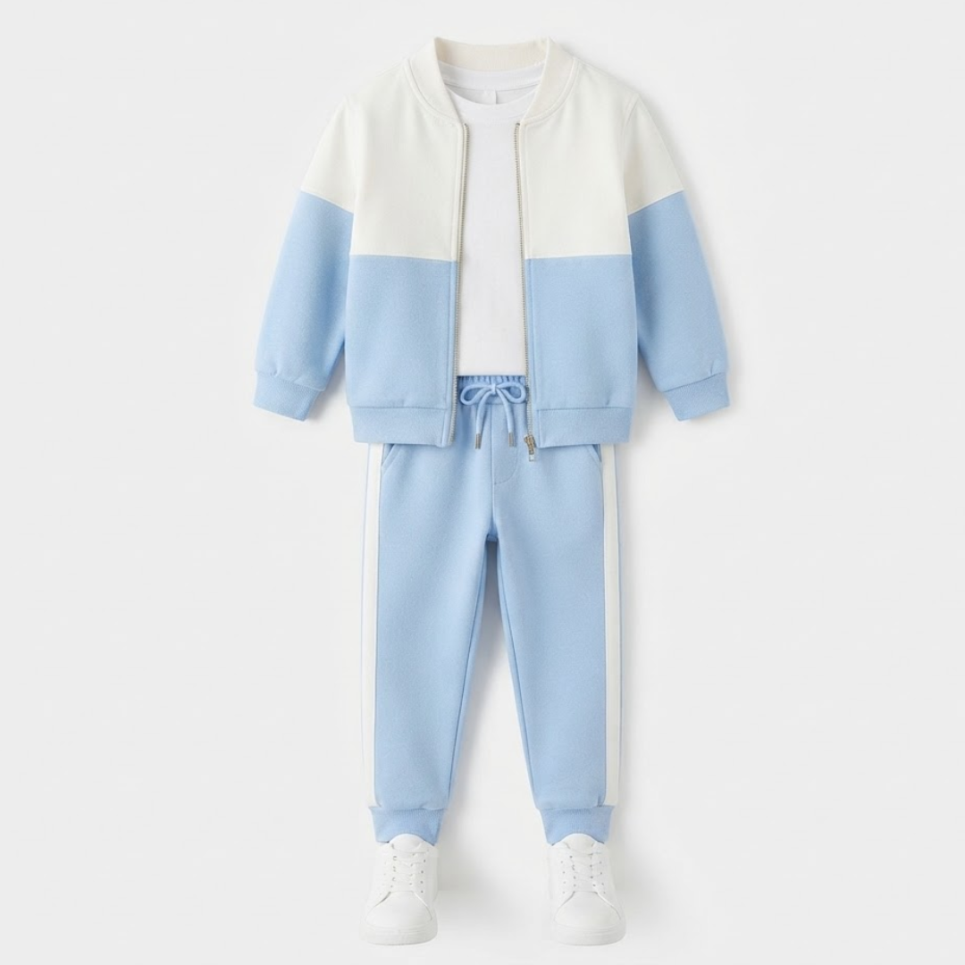 A children's color-blocked two-piece tracksuit set featuring a light blue and off-white jacket with a white collar, paired with matching light blue jogger pants with white side stripes, styled with a white t-shirt and white sneakers on a light gray background.