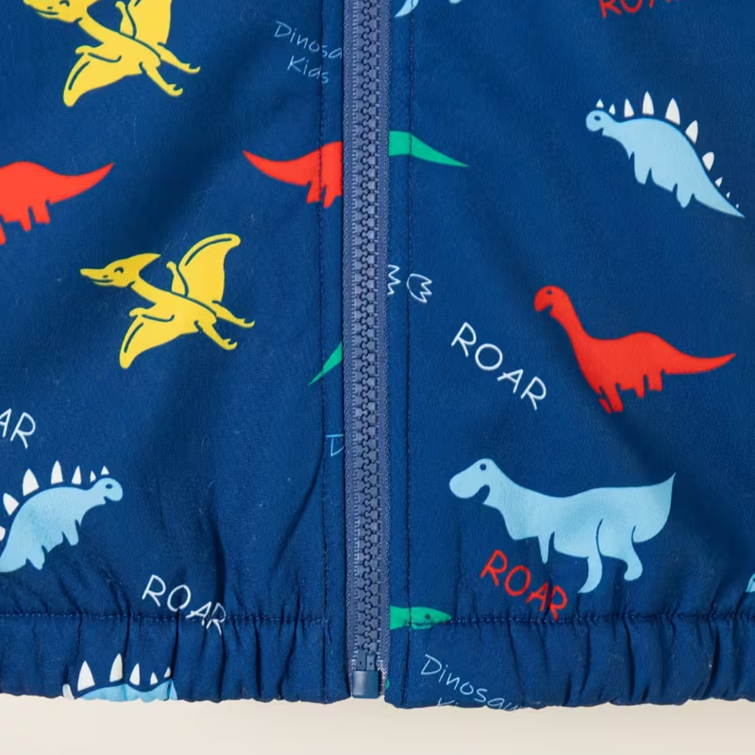 Close-up of a children's zippered jacket or fabric panel in navy blue with a dinosaur print, including yellow, red, green, and light blue dinosaurs, plus the word 'ROAR' repeated on a white background.