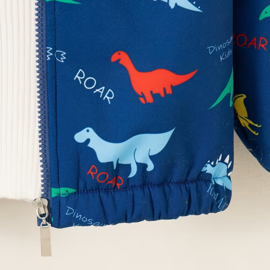 Close-up of a children's curtain panel with a blue background and a colorful dinosaur print, including red, light blue, green, and yellow dinosaurs with the word 'ROAR' in white and red text. A silver zipper is visible on the left side.