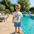 Child wearing sunglasses and a t-shirt with a lobster design by a poolside.