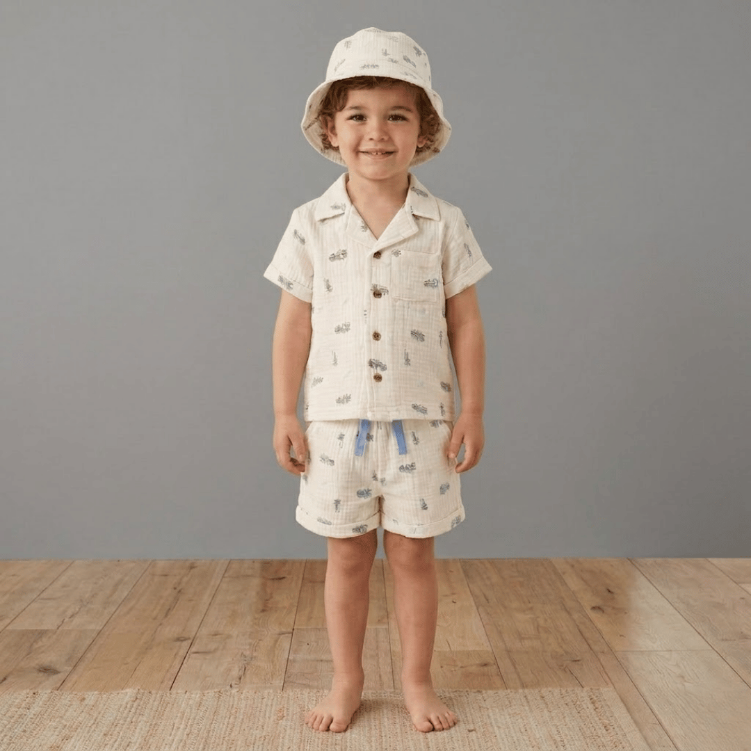 Child wearing a matching shirt and shorts set with a hat on a wooden floor.