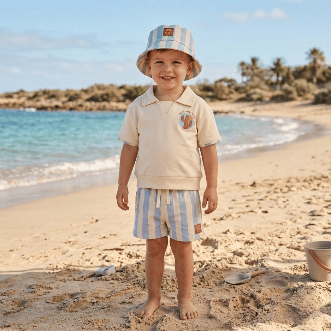 Child in beach attire standing on a sandy beach with ocean and sky in the background