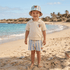 Child in beach attire standing on a sandy beach with ocean and sky in the background