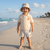 Child on a beach wearing a striped hat and shorts with a logo on a polo shirt.