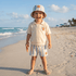 Child on a beach wearing a striped hat and shorts with a logo on a polo shirt.
