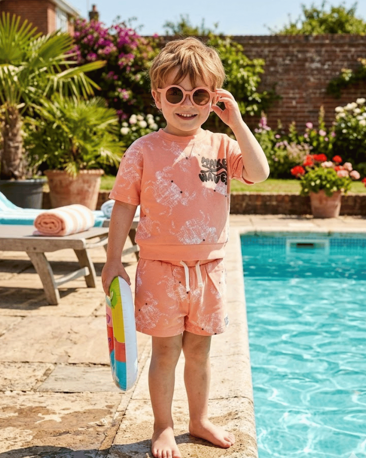 Child in pink swim set standing by a pool with sunglasses on