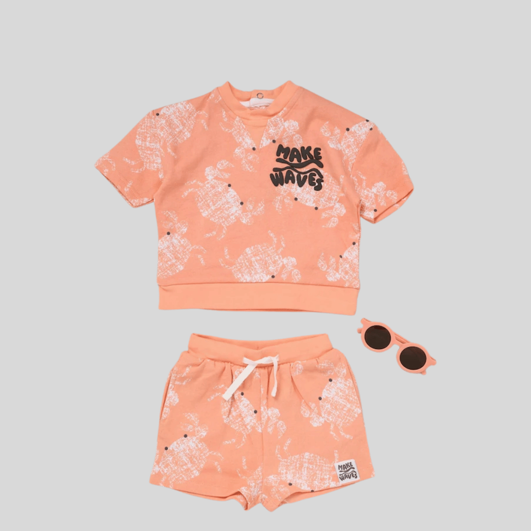 Peach-colored children's outfit with floral pattern and sunglasses on a gray background