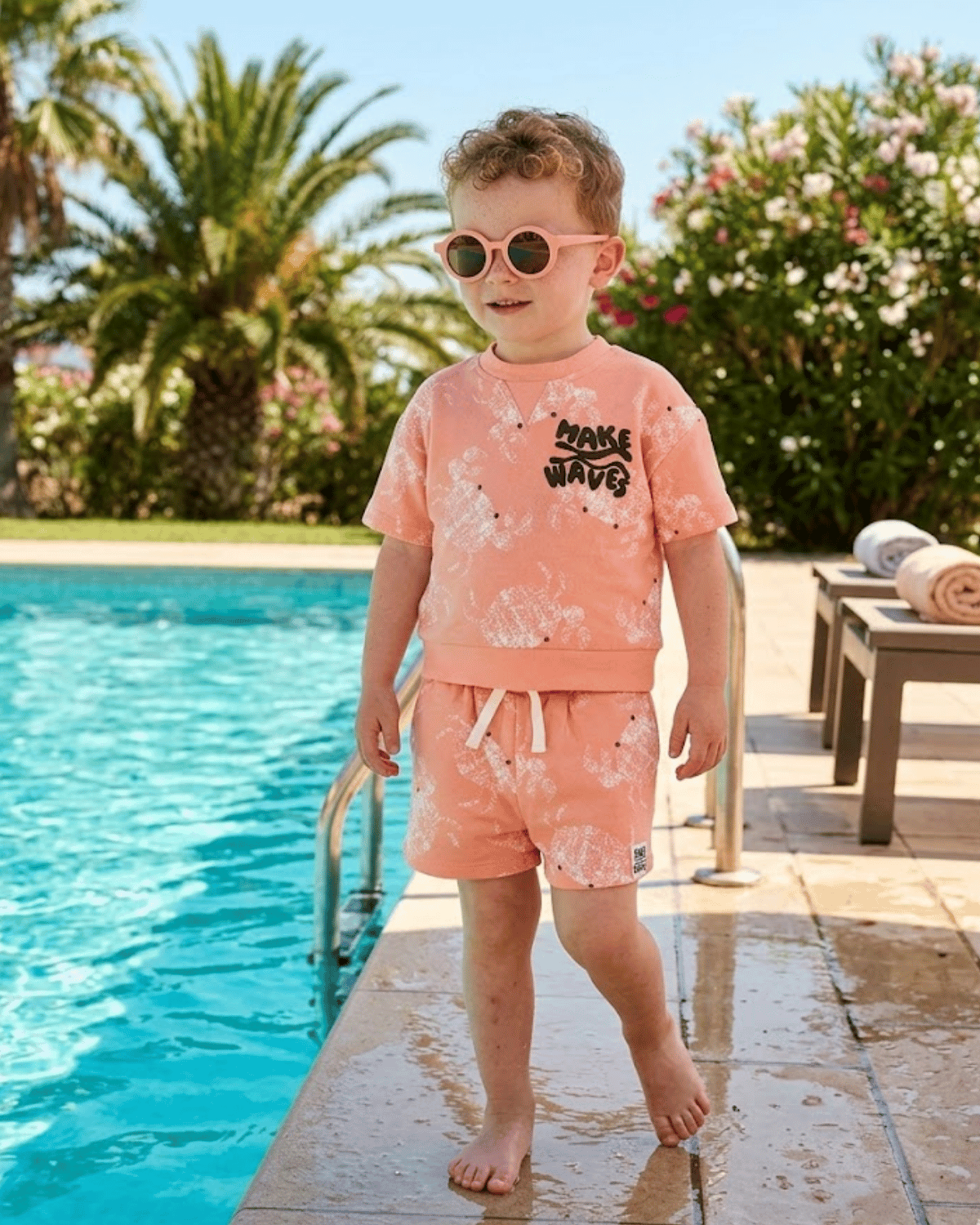 Child in a pink outfit standing by a pool with sunglasses on