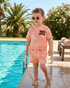 Child in a pink outfit standing by a pool with sunglasses on