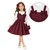A young girl models a two-piece outfit consisting of a white long-sleeve top and a burgundy floral patterned pinafore dress with matching bows. She is holding a matching small handbag, and a circular inset provides a close-up of the dress bodice and bow details.