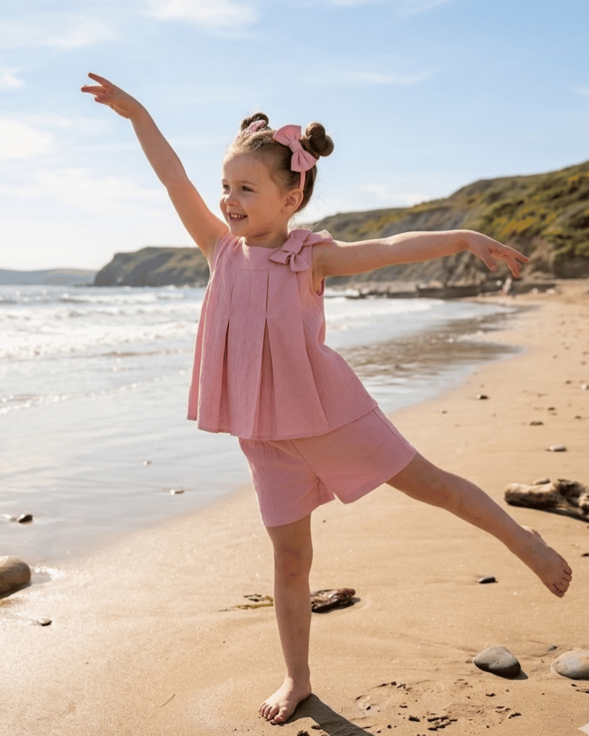 Young girl in a pink dress playing on a sandy beach with ocean and cliffs in the background