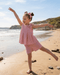 Young girl in a pink dress playing on a sandy beach with ocean and cliffs in the background