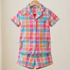 A two-piece children's pajama set featuring a short-sleeve button-front top and matching shorts in a pastel plaid pattern of pink, blue, orange, and white, hanging on a wooden hanger against a plain beige background.