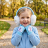 Young girl smiling outdoors in a park during autumn, wearing a light blue fleece jacket with Disney Frozen Elsa earmuffs and matching fingerless gloves with her hands resting on her cheeks