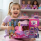 A young girl with a ponytail smiles while holding a boxed Disney Princess toy set in a bright room. The packaging shows a pink castle playset and character figures, with Disney Princess branding clearly visible on the front.