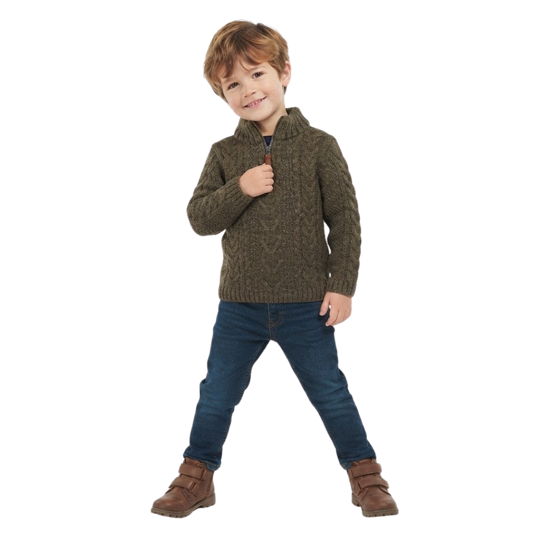 A young boy smiling while wearing an olive green cable-knit quarter-zip sweater, dark denim jeans, and brown boots against a plain white background.