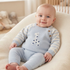 A smiling baby sitting in a soft chair, wearing a light blue knitted sweater with striped sleeves and a giraffe graphic, along with matching blue pants.