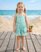 Young girl in a floral dress standing on a wooden deck by the beach.
