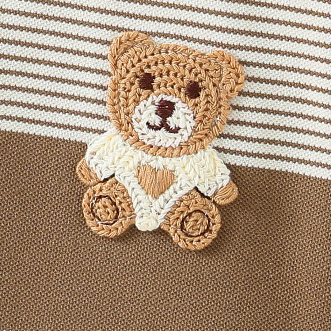 Crocheted teddy bear with a white blanket on a brown and white striped background