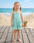 Young girl in a floral dress standing on a wooden deck by the beach.