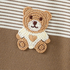 Crocheted teddy bear with a white blanket on a brown and white striped background